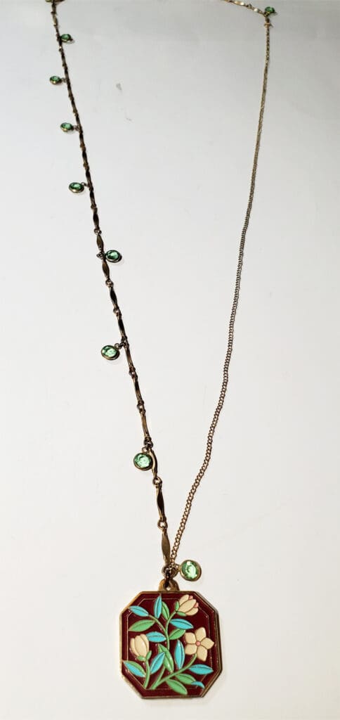 Gold necklace featuring an octagonal pendant with multicolored floral design, accented by green stone details along the chain.