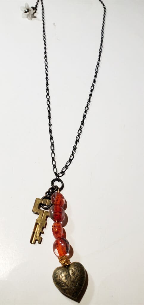 Black chain necklace featuring a vintage key, colorful glass beads, and a decorative heart-shaped pendant, symbolizing love and mystery.