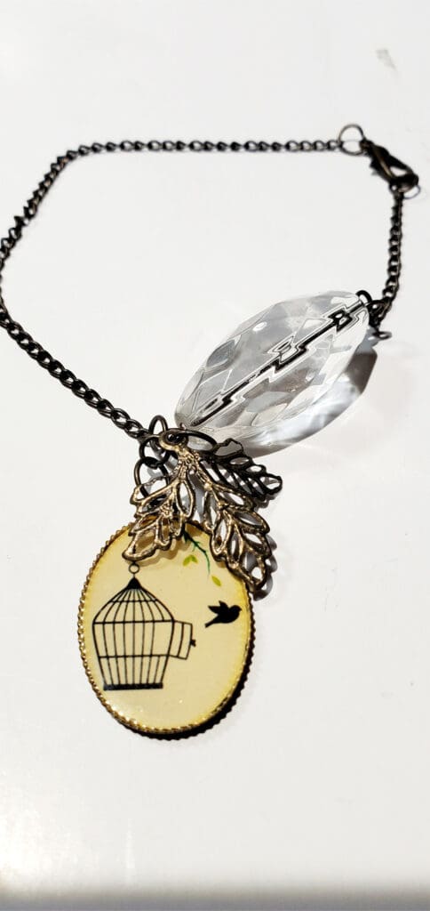 Vintage-style necklace featuring a decorative birdcage pendant, embellished with a leaf design and a clear crystal accent.